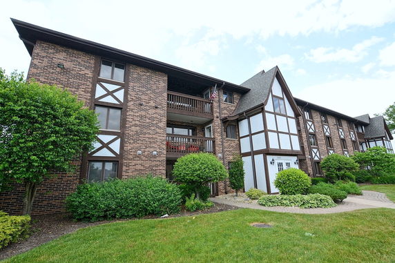 Front view of a three-story brick apartment building with balconies and a gabled roof.