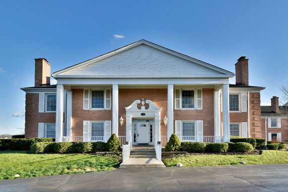 Front view of a two-story house with brick facade, white columns, and a gabled roof.