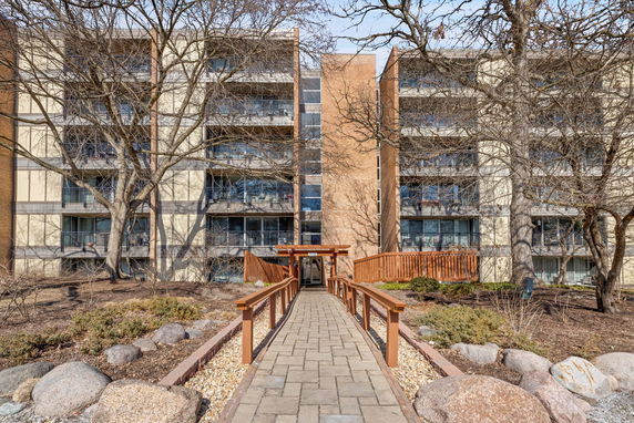 Front view of a multi-story apartment building with balconies and a stone pathway leading to the entrance.