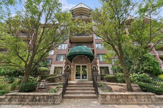 Front view of a multi-story apartment building with balconies and a green awning over the entrance.