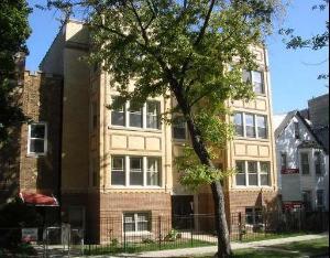 Front view of a multi-story apartment building with a tree in front.