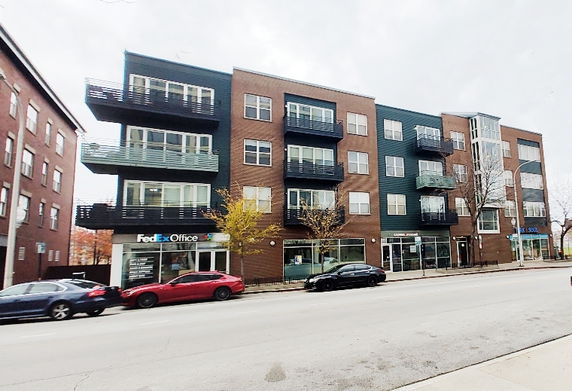 Front view of a four-story building with balconies and ground-floor retail spaces.