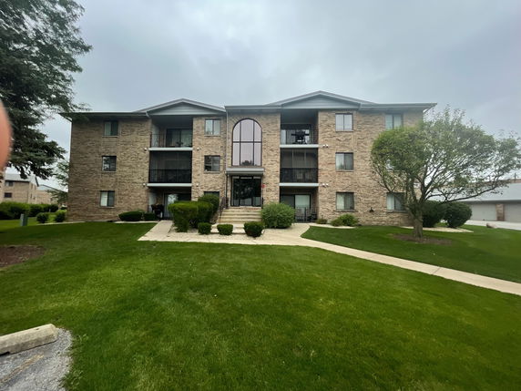 Front view of a multi-story brick apartment building with central balconies.
