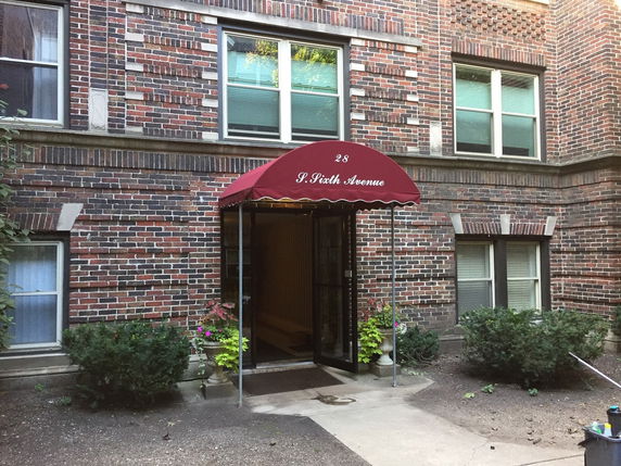 Front view of a brick apartment building with a red canopy above the entrance.