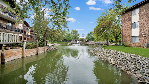 View of apartment buildings near a small lake with a fountain.