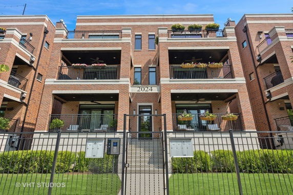 Front view of a multi-story brick building with balconies and gated entry.