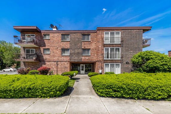 Front view of a three-story brick apartment building with balconies.