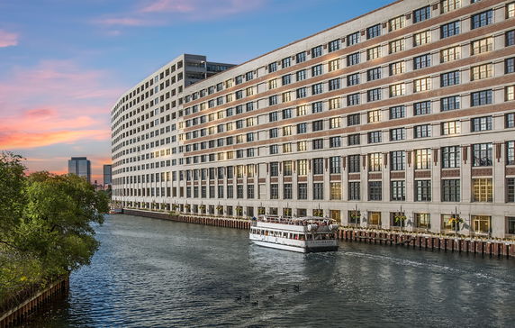 Front view of a multi-story building along a river with a sunset in the background.