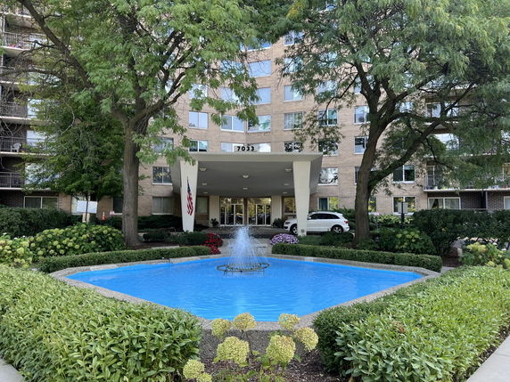 Front view of a multi-story building with a water fountain and greenery.
