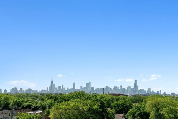 Panoramic view of a city skyline with tall buildings visible in the distance over a lush green landscape.