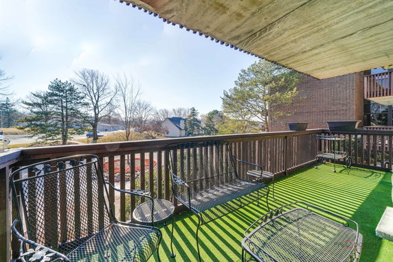 Balcony with metal furniture overlooking surrounding residential area with trees and houses.