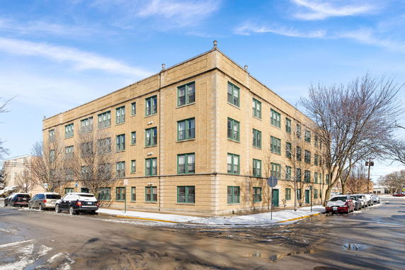 Front view of a four-story brick apartment building on a street corner.