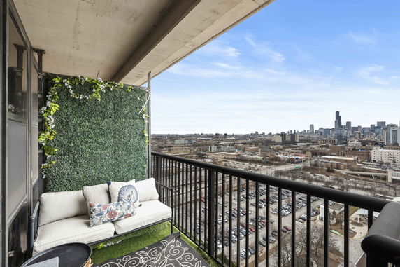 Balcony with seating and decorative greenery, overlooking a city skyline.