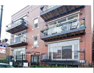 Front view of a three-story building with balcony railings and brick exterior.