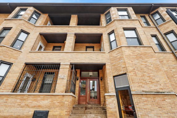 Front view of a multi-story brick building with balconies and stairs leading to a double door entrance.
