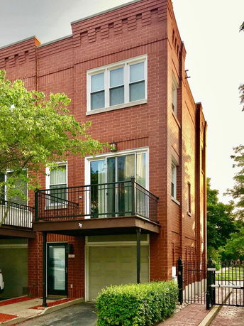 Front view of a three-story brick building with a balcony and garage.