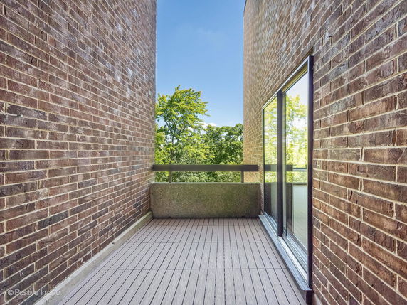 Balcony view with brick walls and glass sliding door overlooking greenery.