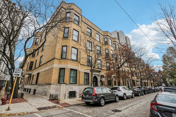Front view of a multi-story apartment building on a city street with parked cars.