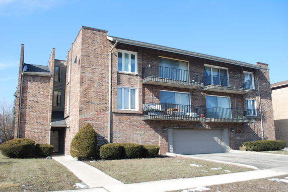Front view of a multi-story brick apartment building with balconies and garage.