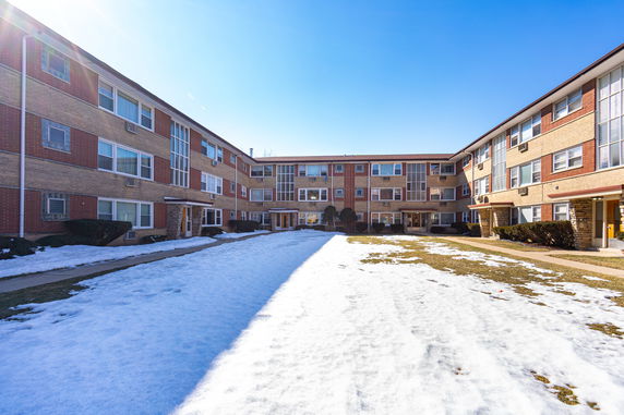 Front view of a three-story apartment building with red and beige brick exterior, featuring multiple windows and snow-covered ground.