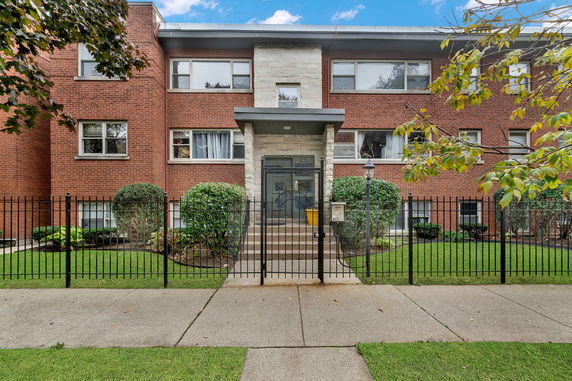 Front view of a two-story brick building with a gated entrance and steps leading to the main door.