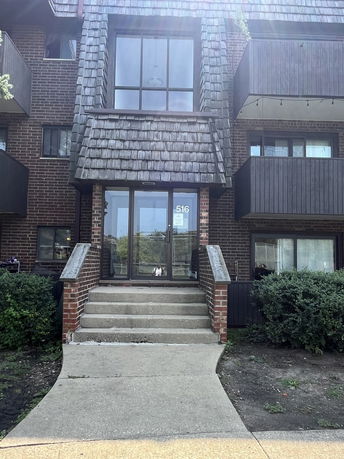 Front view of a multi-story brick building with shingled upper facade and glass entrance doors.