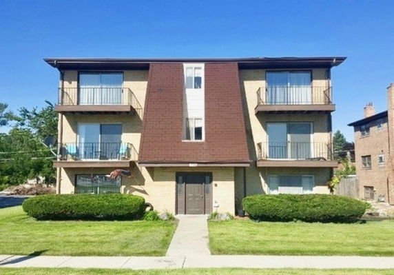 Front view of a three-story residential building with balconies and a sloped roof.