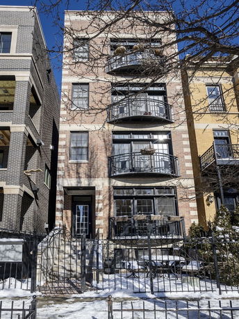 Front view of a multi-story building with balconies and a gated entrance.