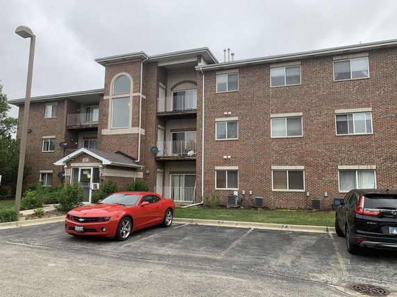 Front view of a three-story brick apartment building with balconies.