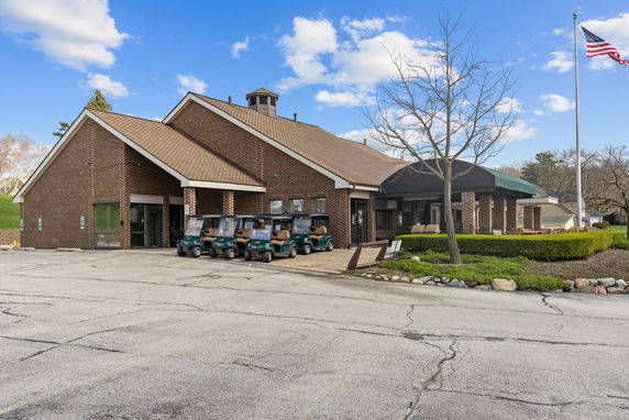 Front view of a brick building with a sloped roof and several golf carts parked in front.