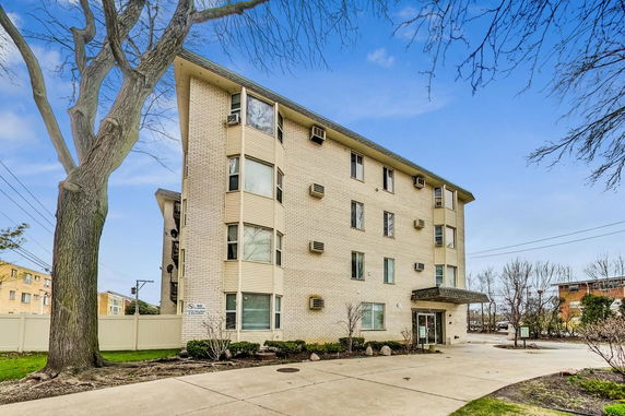 Front view of a multi-story apartment building with a light brick exterior.