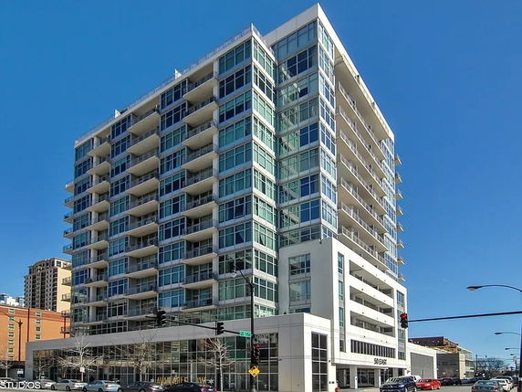 Front view of a multi-story modern apartment building with glass balconies.