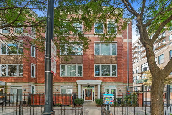 Front view of a multi-story brick apartment building with large windows and a gated entrance.
