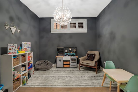 Interior view of a children's play area with a chair, table, toy kitchen set, and shelves with toys.