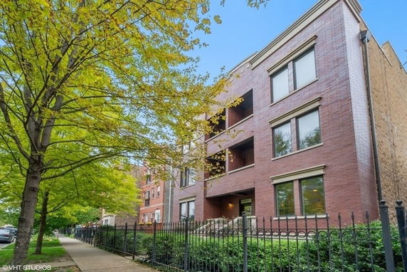 Front view of a multi-story brick apartment building with iron fence.