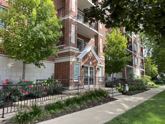 Front view of a multi-story brick apartment building with balconies and landscaped entrance.