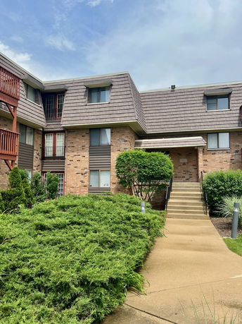 Front view of a multi-story brick apartment building with an entrance staircase.