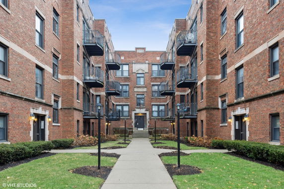 Front view of a multi-story brick apartment building with balconies and courtyard.