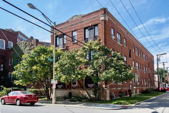 Front view of a three-story brick apartment building on a street corner.