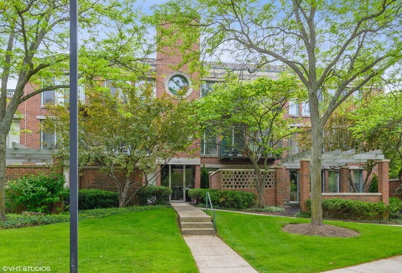 Front view of a brick building with large windows and a landscaped entrance.