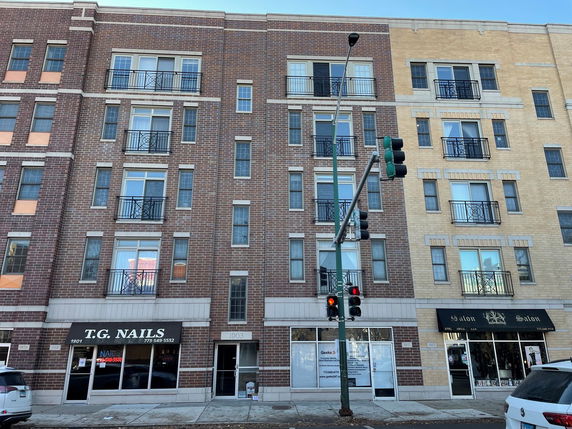 Front view of a multi-story building with brick exterior and multiple balconies, featuring shops at the ground level.