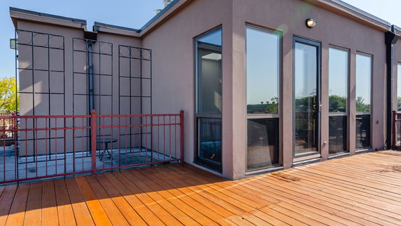 Rooftop area with wooden decking and a metal railing surrounding the space.