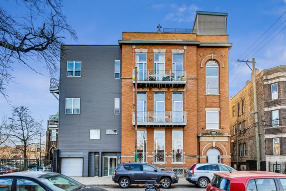 Front view of a multi-story brick building with balconies and modern extensions.