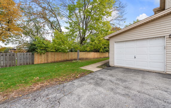 Outdoor view of a garage with a concrete driveway and a wooden fence.