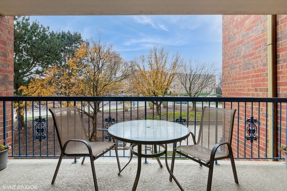 View from a balcony with a glass table and chairs overlooking trees and a distant building.