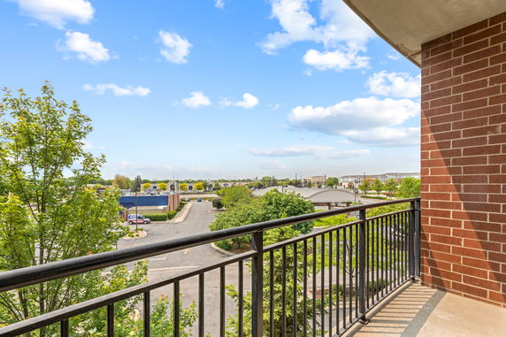 View from a balcony with a metal railing overlooking a parking area and surrounding buildings.