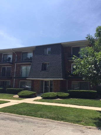 Front view of a three-story brick apartment building with a distinctive sloped roof entrance.
