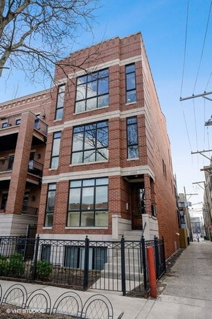 Front view of a three-story brick building with large windows and a gated entrance.