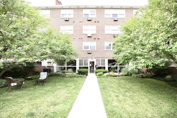 Front view of a multi-story brick building with large windows and a garden path leading to the entrance.