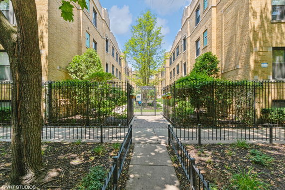 Front view of a brick apartment building with a gated entrance and surrounding greenery.